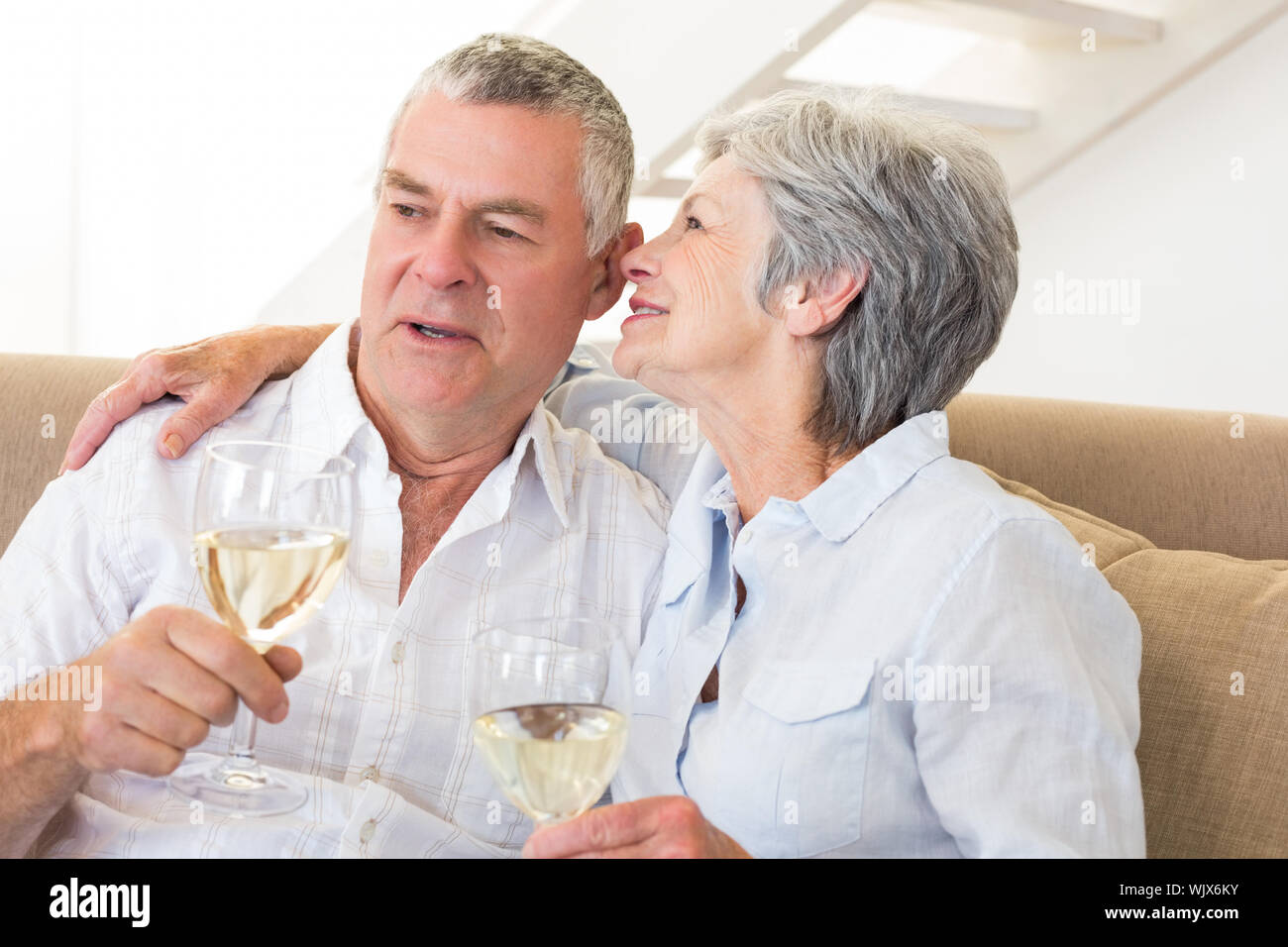 Senior couple sitting on couch drinking white wine à la maison dans la salle de séjour Banque D'Images