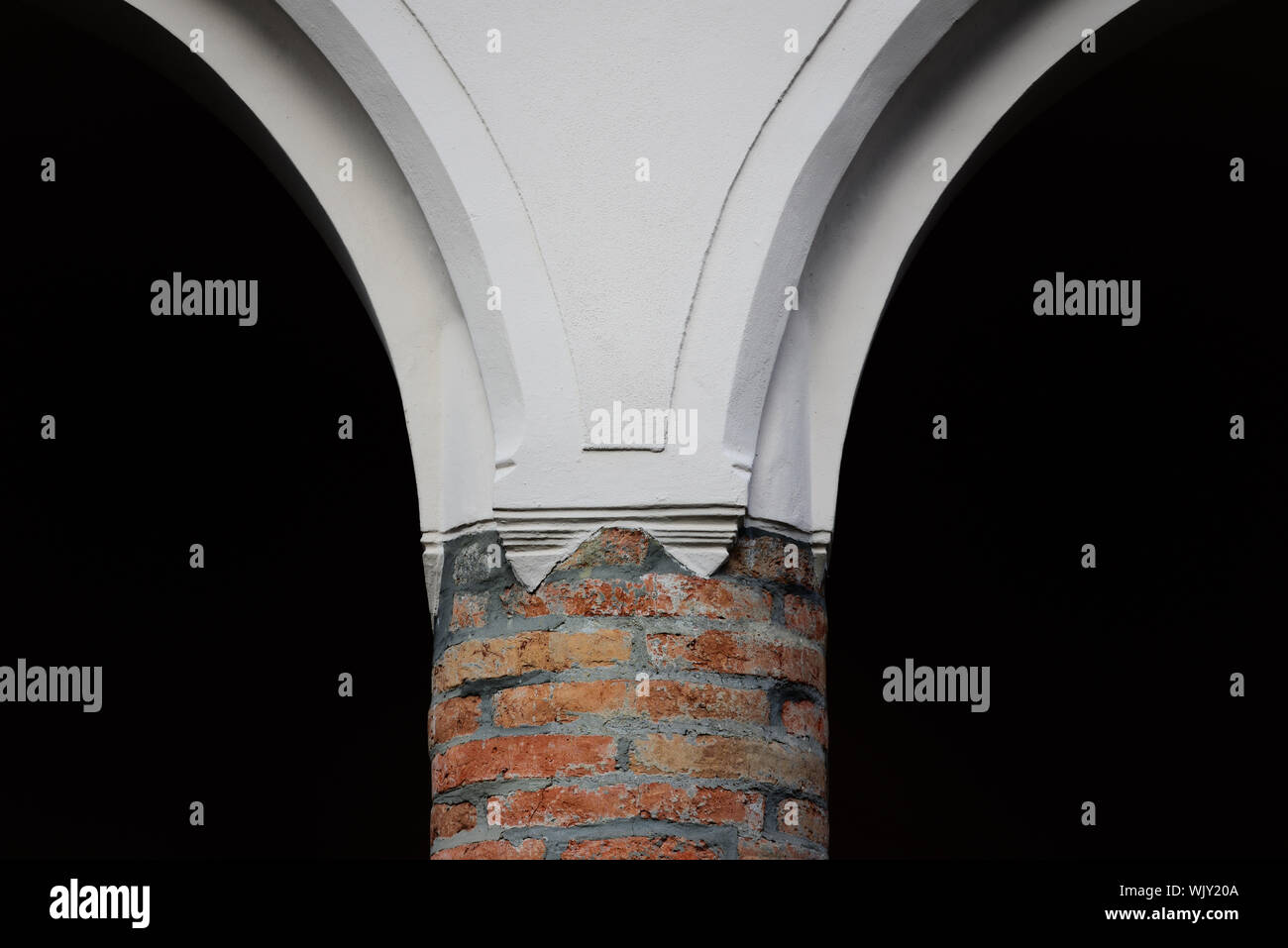 Détail d'un pilier de briques historique placardée avec transition vers le haut, divisant contre un fond sombre au centre du tableau Banque D'Images
