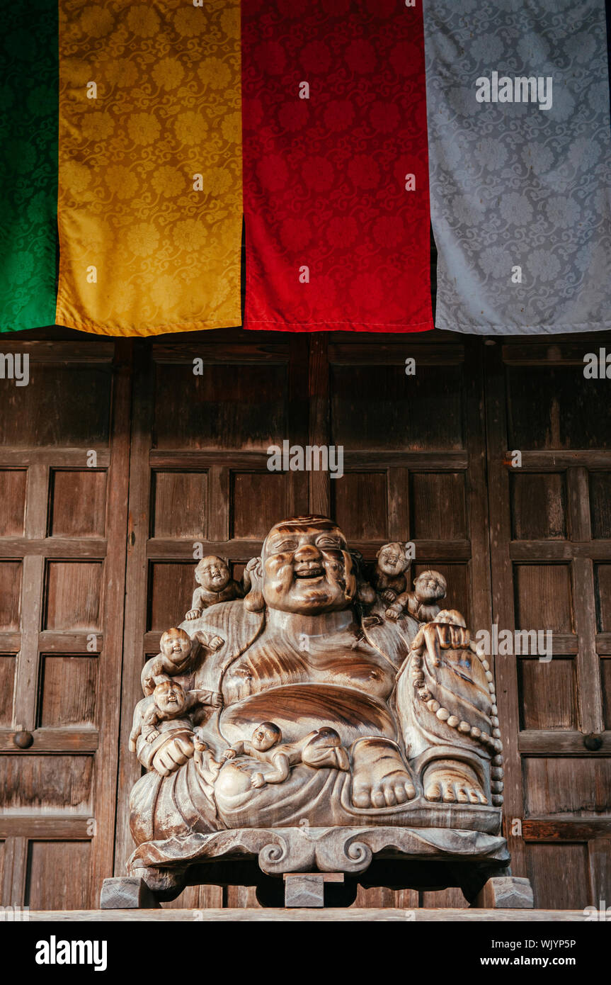 DEC 3, 2018 Yamagata, Japon - Japonais en bois sculpté statue Bouddha souriant sous les drapeaux dans le bouddhisme colorés Yamadera Risshaku ji Banque D'Images