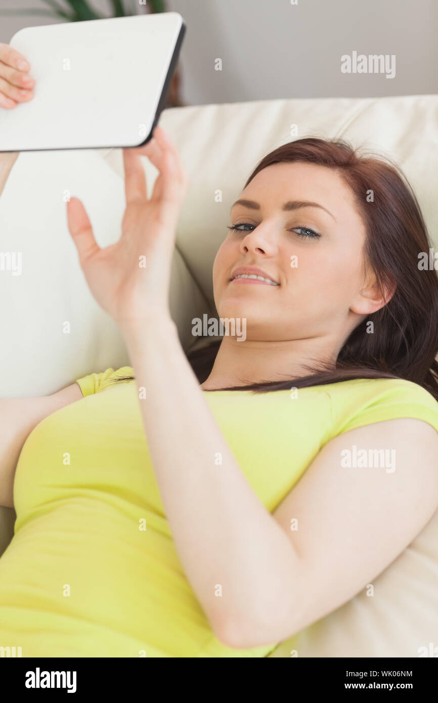 Happy teen girl lying on sofa using a tablet pc Banque D'Images
