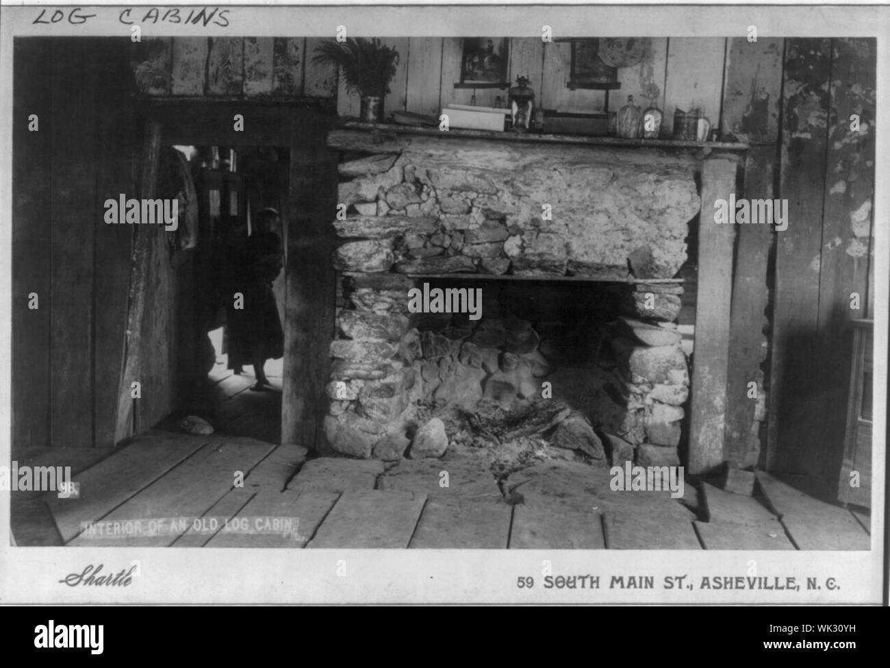 L'intérieur d'une vieille cabane, montre une cheminée et un enfant tenant un petit enfant à l'intérieur de la porte d'une chambre voisine Banque D'Images