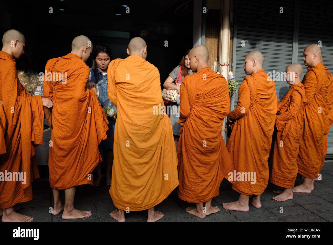 Un groupe de moines bouddhistes à Bangkok, Thaïlande, entassés autour de commerçants sortir sur un matin tôt pour donner des offrandes et demander des bénédictions Banque D'Images