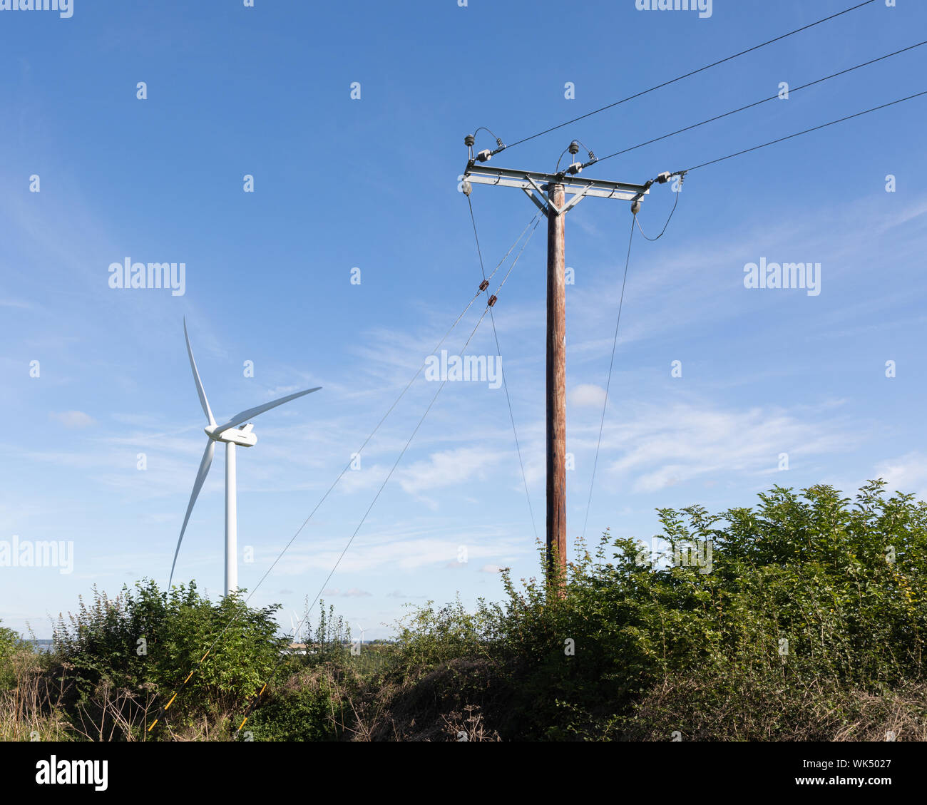 Crick, Northamptonshire, Royaume-Uni: Un poteau électrique en bois se tient devant une éolienne sous un ciel bleu et des nuages chuchotés. Banque D'Images