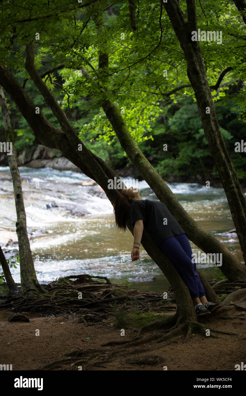 Toute la longueur de Woman Leaning On Tree Trunk à Rivière en forêt Banque D'Images