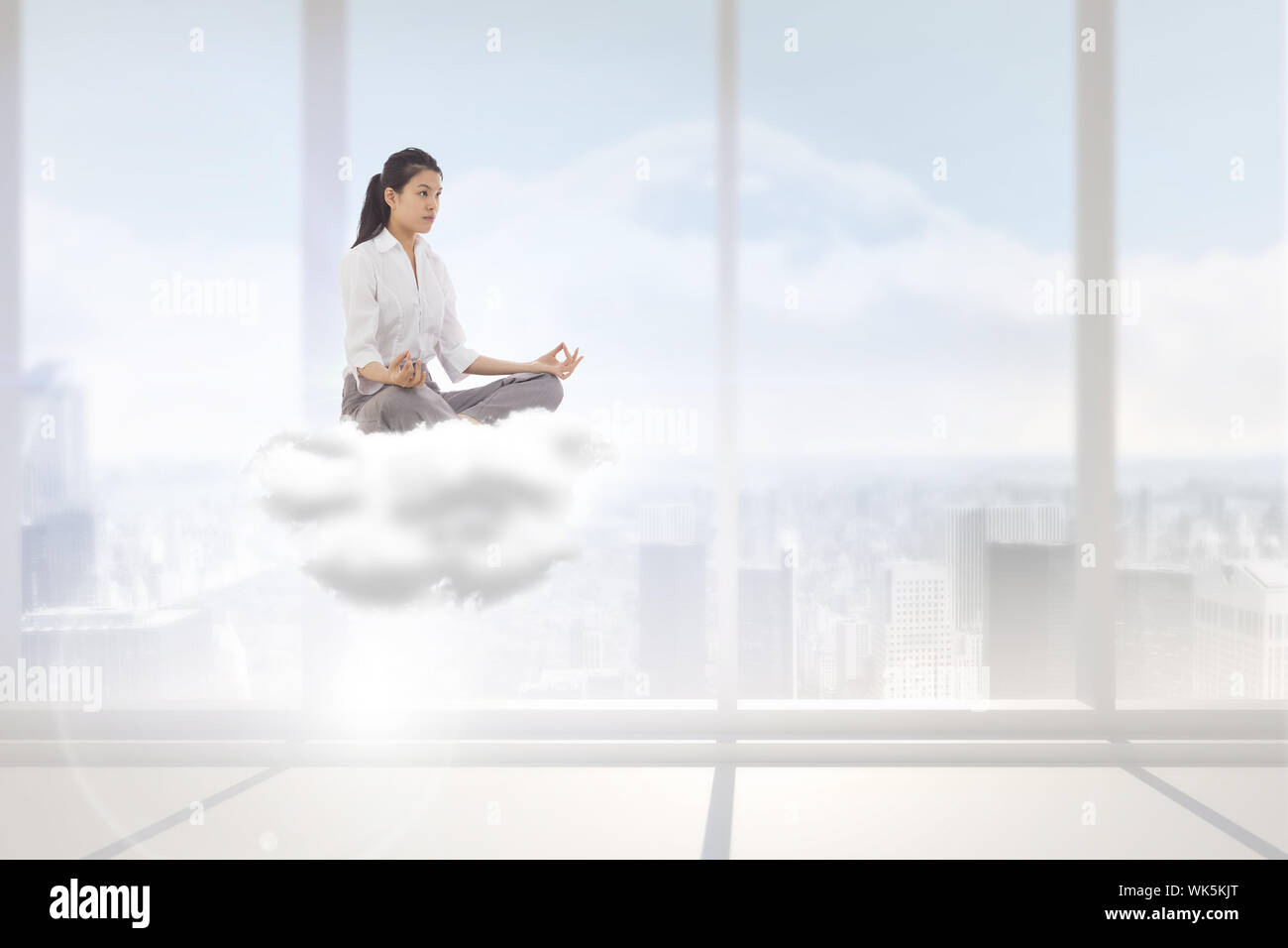 Businesswoman sitting in lotus pose contre chambre blanc brillant avec windows Banque D'Images