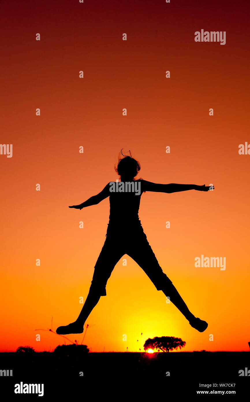 Silhouette d'une jeune femme sautant au coucher du soleil Banque D'Images