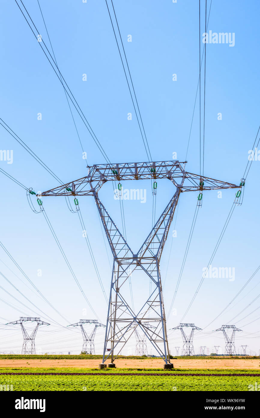 Vue frontale d'un pylône d'électricité dans la campagne française avec des dizaines d'autres pylônes au loin sous un ciel bleu clair. Banque D'Images