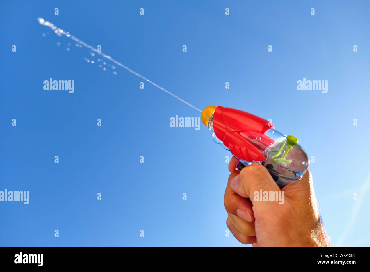 Pistolet à eau colorés à la pulvérisation d'un jet d'eau dans un homme de race blanche main devant le ciel bleu d'un jour d'été ensoleillé Banque D'Images