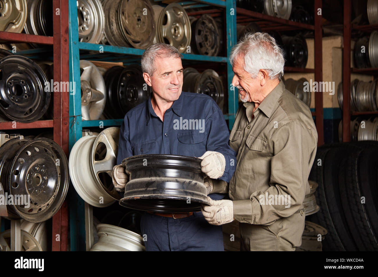 Deux mécaniciens avec jantes de roue de voiture pour les changements de stock de pièces détachées d'un atelier de réparation de voiture Banque D'Images