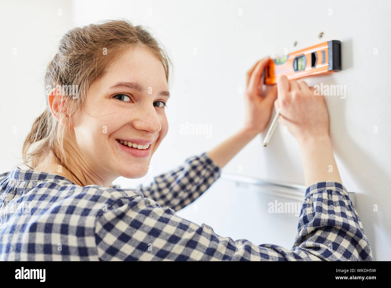 Jeune femme comme DIY home improvement pendant la mesure avec le niveau à bulle sur le mur Banque D'Images