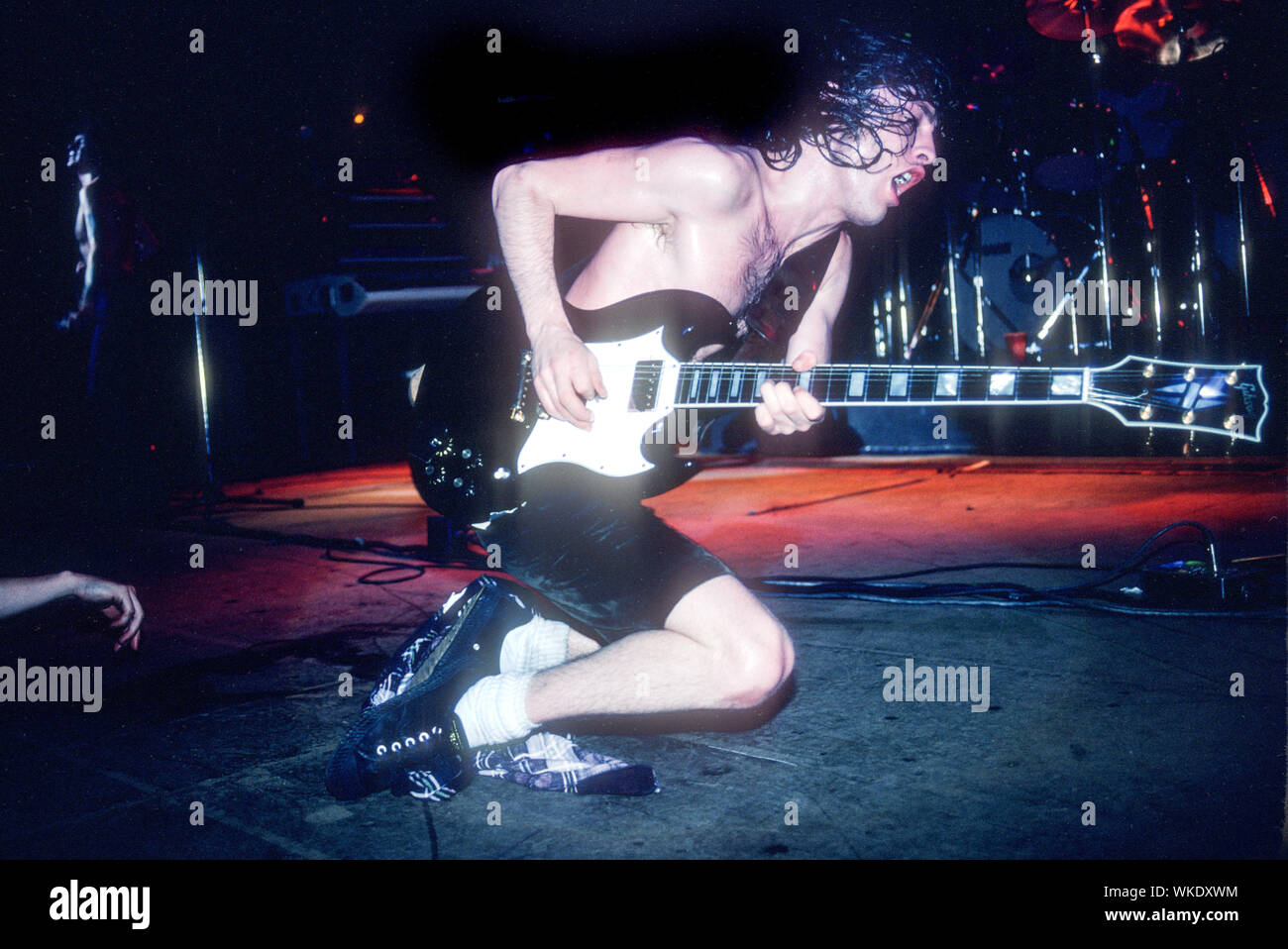 Angus Young de AC/DC joue de la guitare sur ses genoux sur scène au Palladium Theater à New York en juin 1979. Il y a une part visible sur la gauche. Banque D'Images