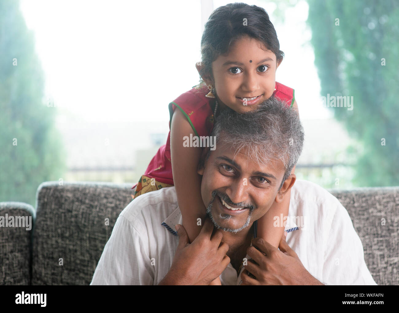 Heureux famille indienne à la maison. Asian father piggyback sa fille, assise sur un canapé. Le parent et l'enfant de vie intérieure. Banque D'Images