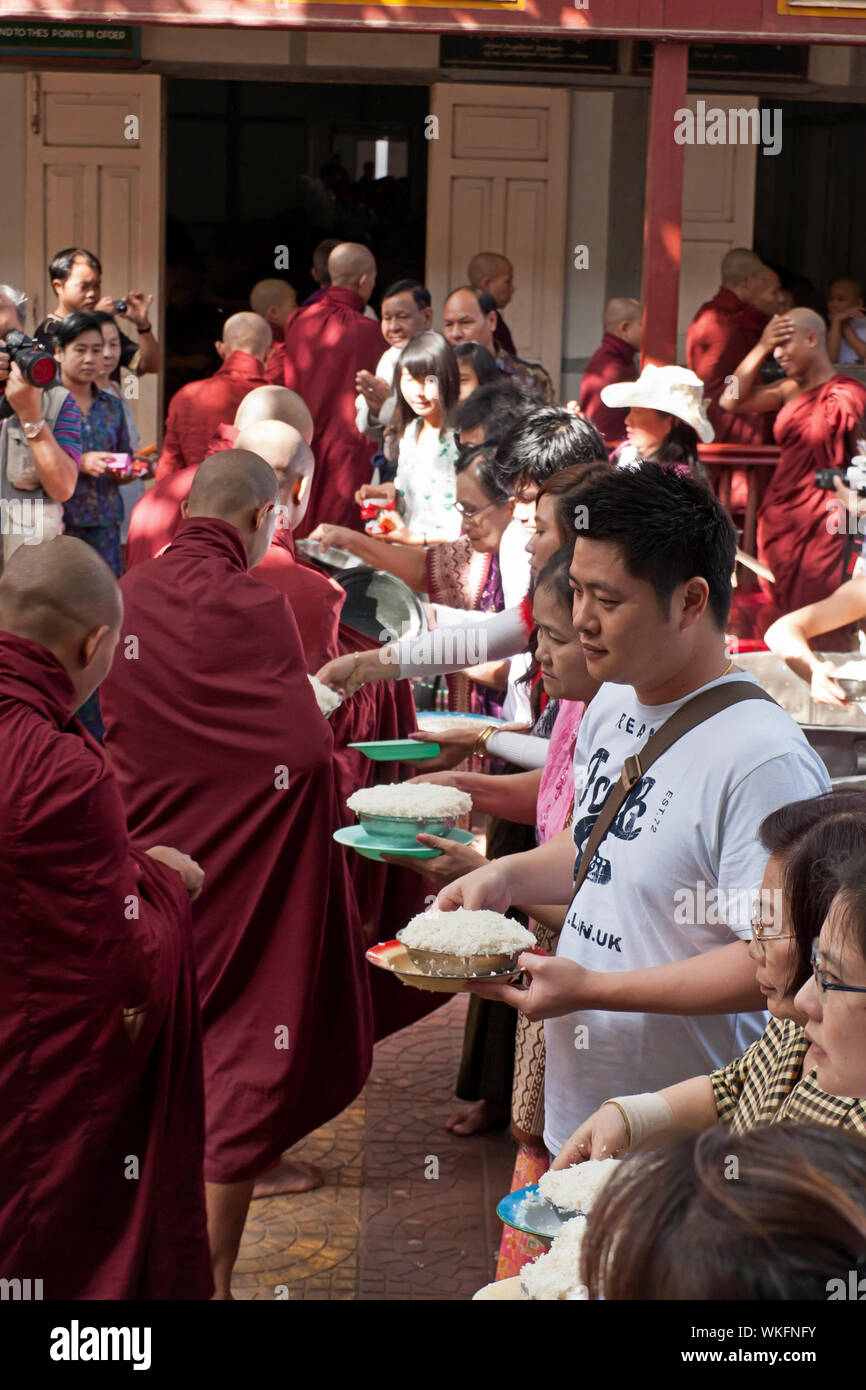 Les touristes distribuant de la nourriture pendant le plus grand déjeuner de moines bouddhistes au monde dans le monastère de Mahagandayon, Mandalay Banque D'Images