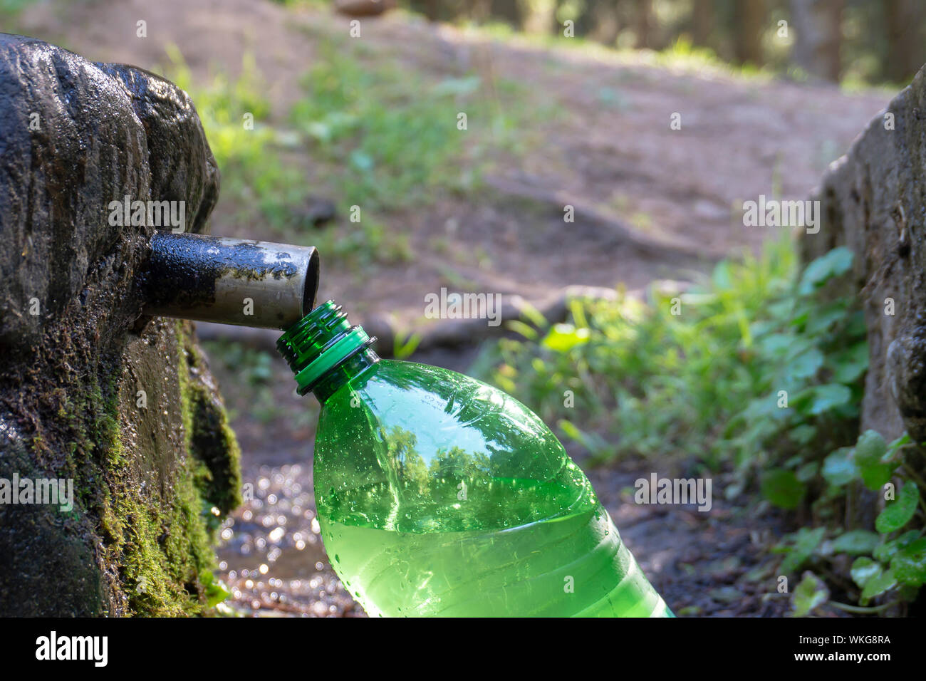 Un remplissage propre et fraîche en plastique vert bouteille d'eau à la fontaine dans un tuyau plein air rock à la campagne dans une vue en gros plan Banque D'Images