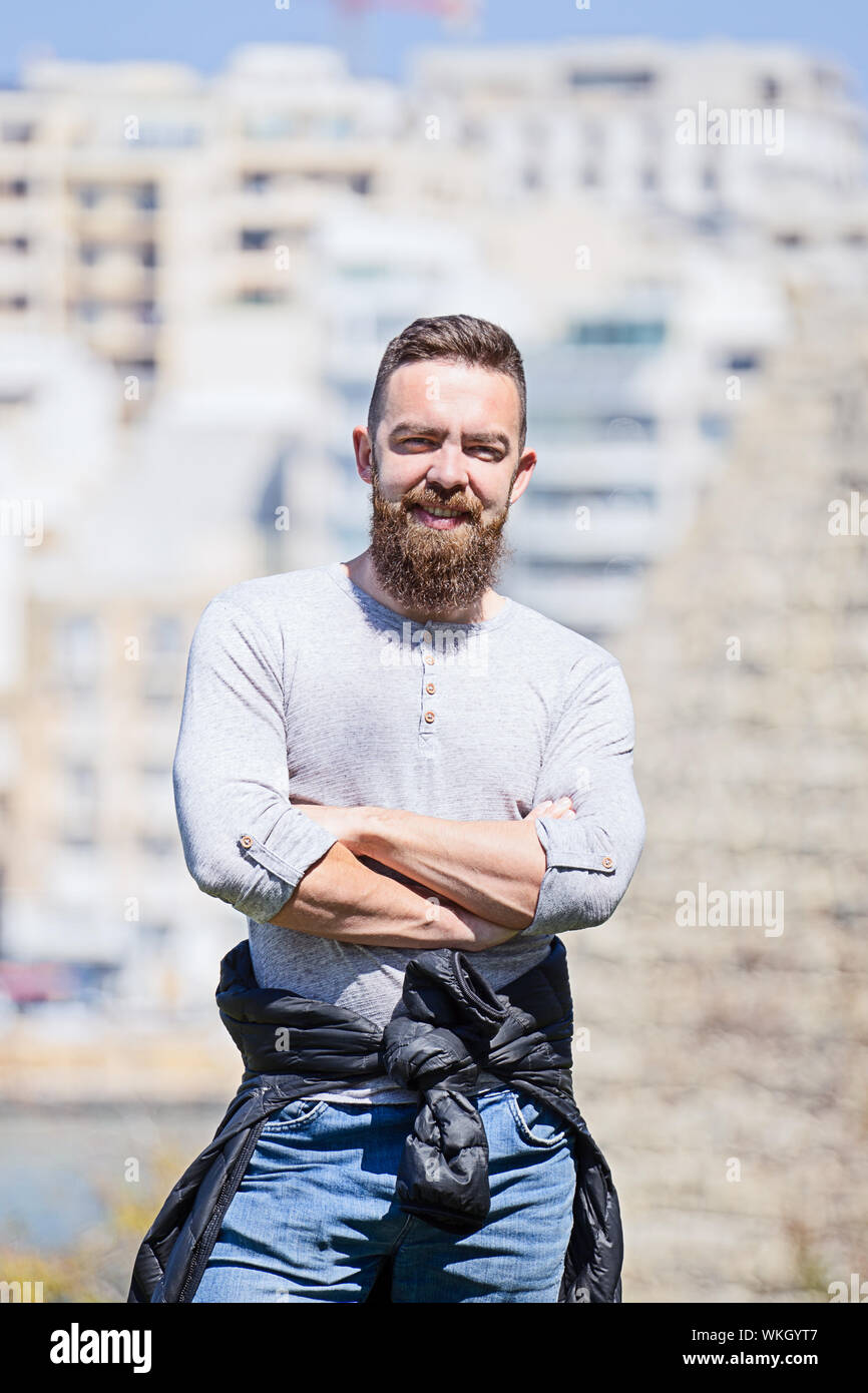 Portrait of caucasian barbu with arms crossed standing outdoors, smiling at camera Banque D'Images