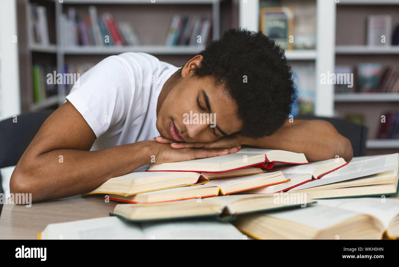 Épuisé afro guy dormir sur books in library Banque D'Images