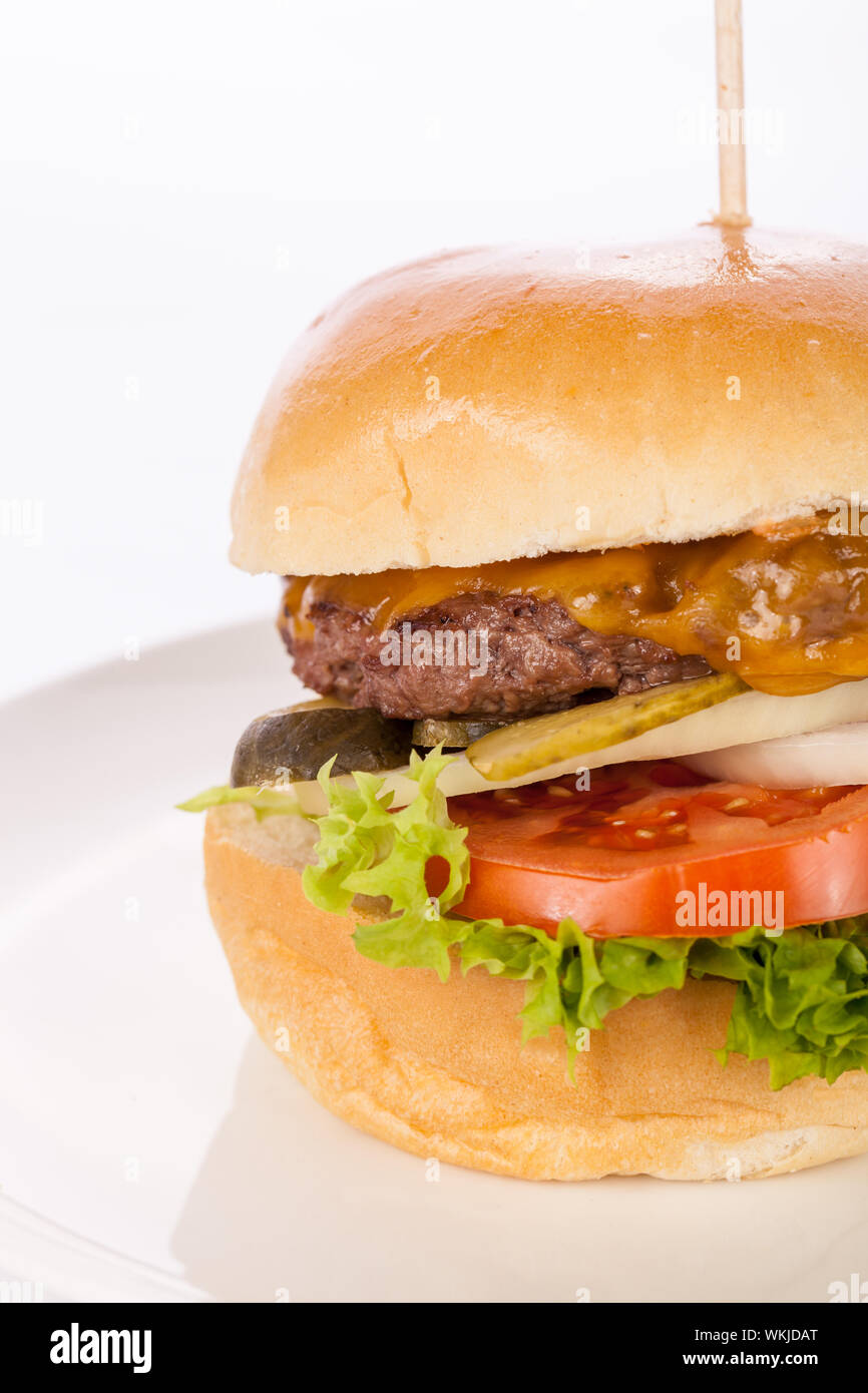 Savoureuse traditionnelle cheeseburger avec un sol recouvert de patty de boeuf fromage fondu et servi avec des rondelles d'oignon, tomate et laitue frisée sur un roun Banque D'Images