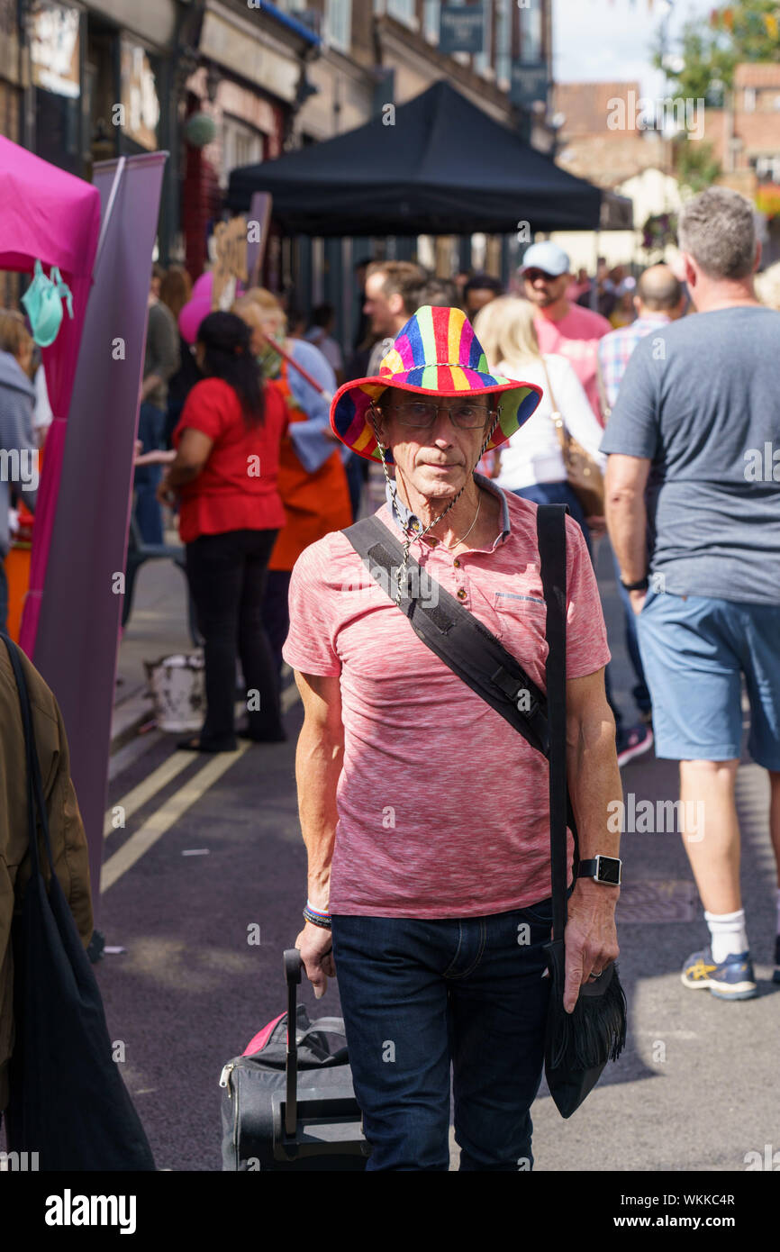 Homme marchant dans une rue portant un chapeau multicolore et un tee-shirt rose, Fossgate Festival, York, North Yorkshire, Angleterre, Royaume-Uni. Banque D'Images