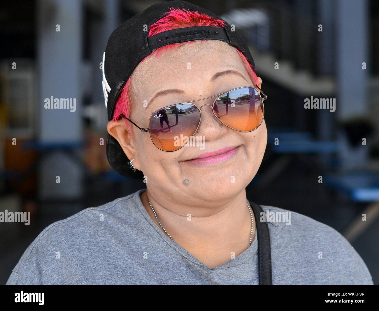 Femme chinoise de Malaisie avec les cheveux teints rouge porte une casquette de baseball inversée en miroir et des lunettes de soleil et de sourires pour l'appareil photo. Banque D'Images
