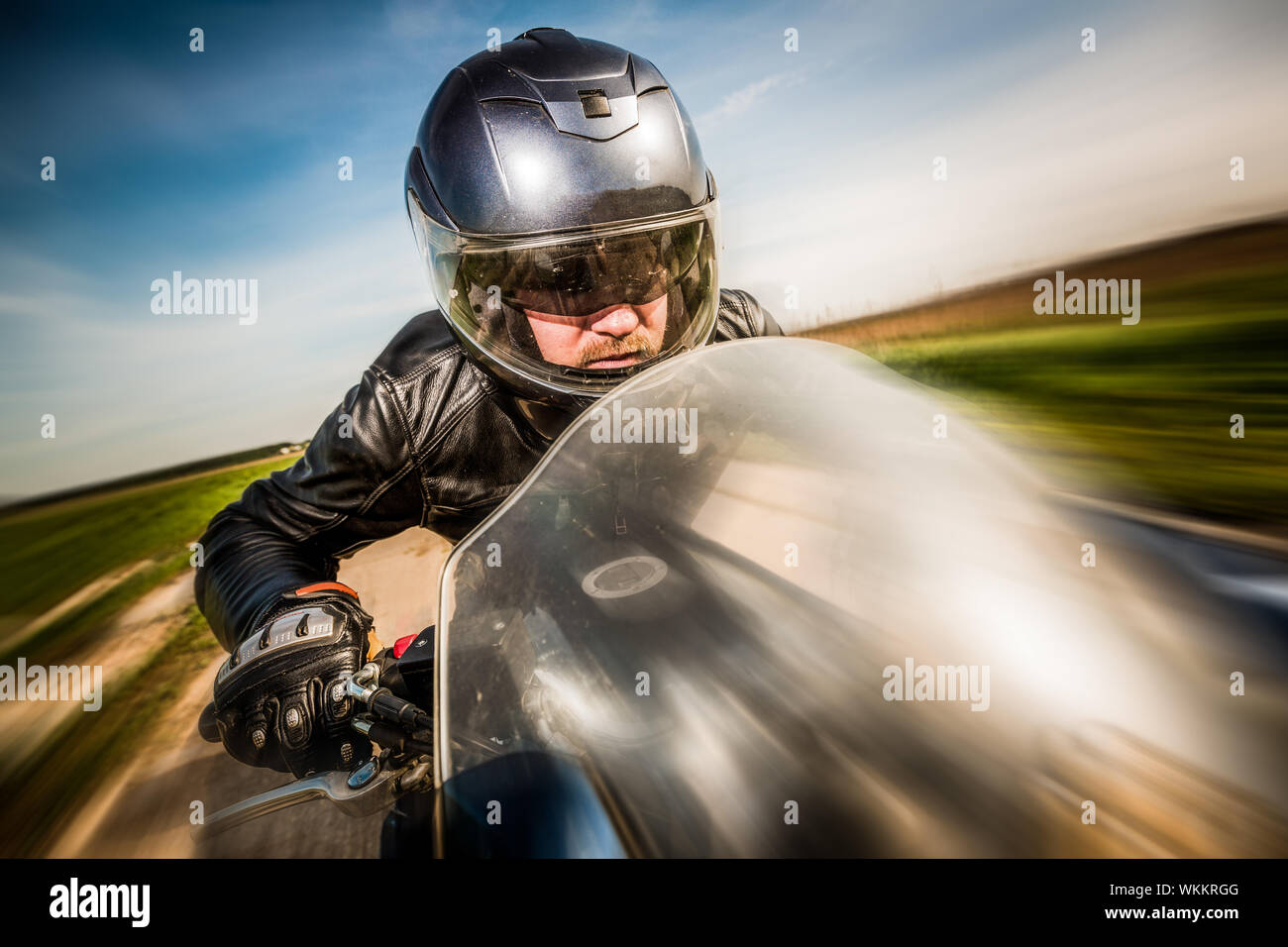 Biker dans casque et blouson de cuir racing sur la route Banque D'Images