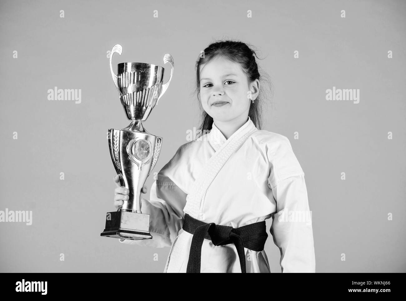 Petite fille gagnant dans gi sportswear. pratiquer le Kung Fu. enfance heureuse. sport succès en combat singulier. girl avec champion cup. Les arts martiaux et l'activité de l'énergie. knockout. Tout est possible. Banque D'Images