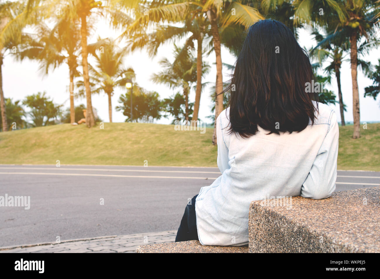 Vue arrière de la femme aux cheveux noirs assis sur les mesures par la route contre des palmiers Banque D'Images