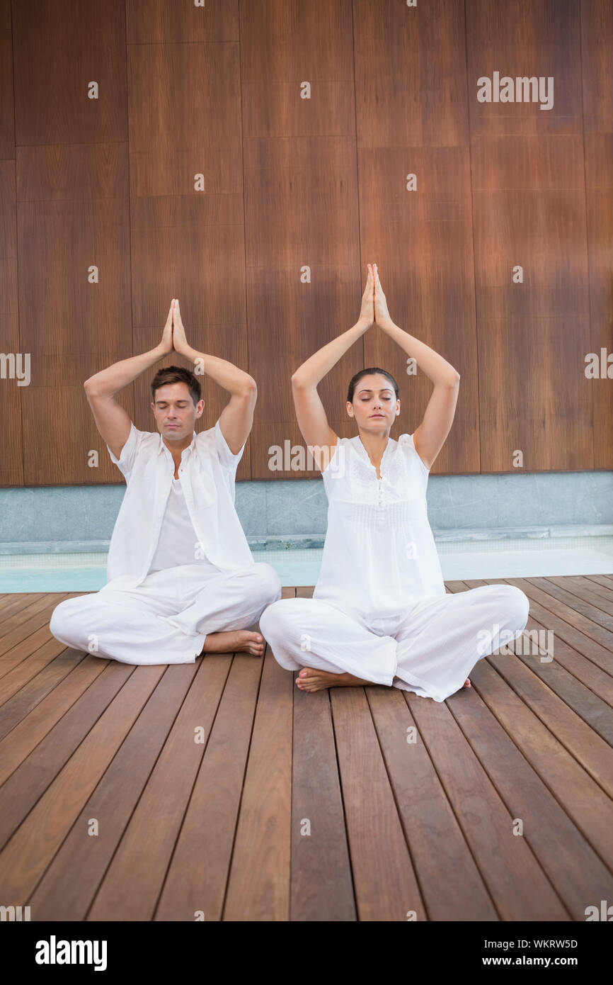 Beau couple en blanc assis dans lotus posent avec les mains ensemble dans health spa Banque D'Images