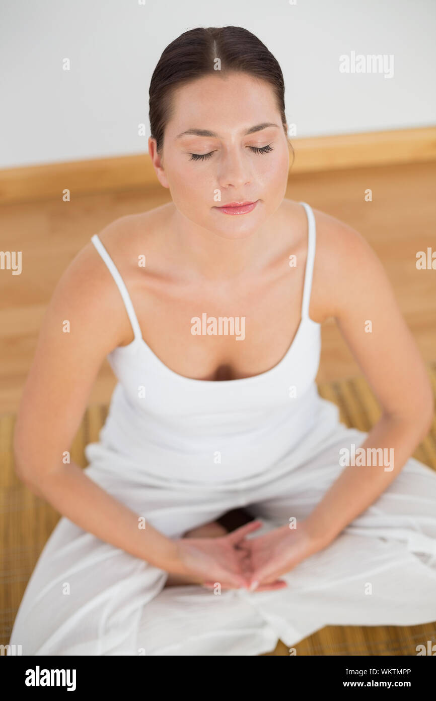 Woman sitting in lotus pose avec les yeux fermés dans une salle blanche Banque D'Images