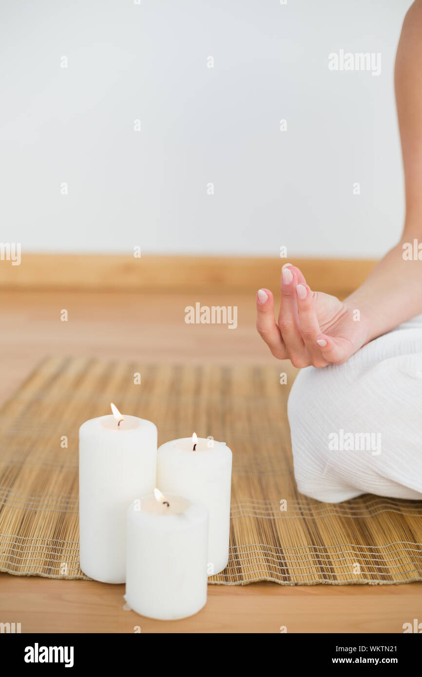 Woman sitting in lotus pose à côté de bougies blanches dans une salle blanche Banque D'Images