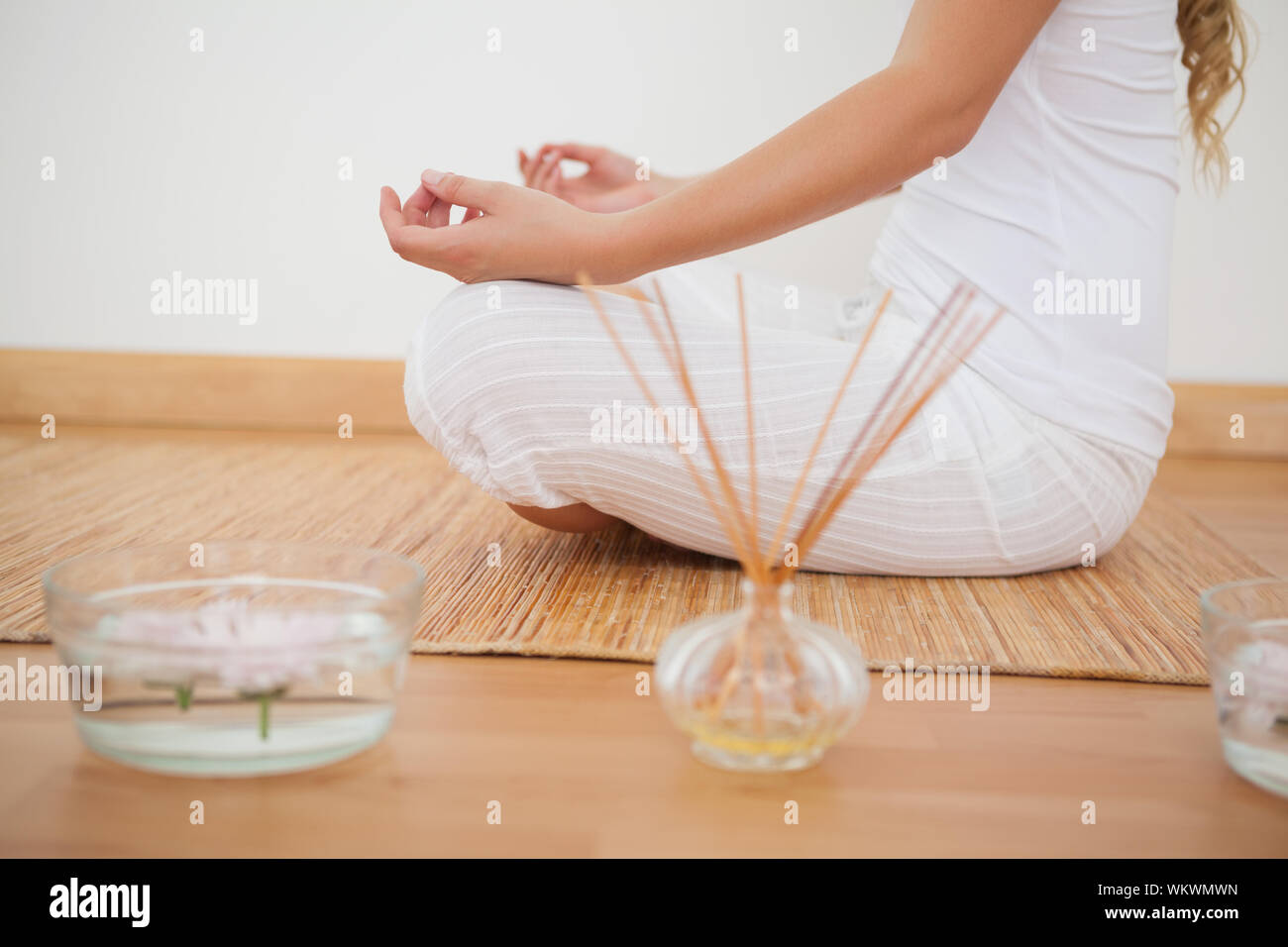 La femme assise en lotus posent sur des panneaux de nattes de bambou à la maison contre un mur blanc Banque D'Images