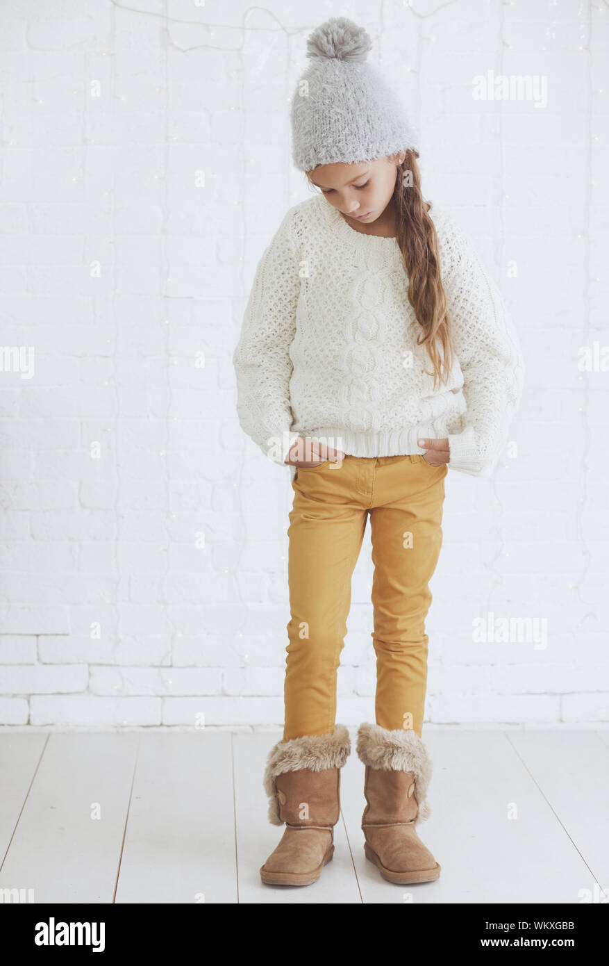 Cute girl 8-9 ans portant des vêtements d'hiver à la mode tricot présentant plus de white brick wall Banque D'Images