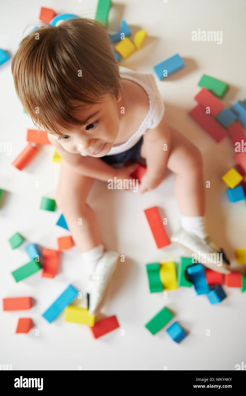 Baby Girl s'asseoir sur fond blanc avec des briques colorées toys Banque D'Images