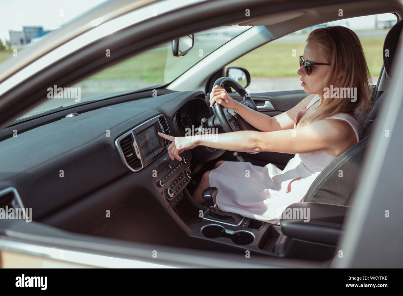 Femme au volant d'une voiture, sélectionne la navigation sur écran d'affichage s'allume, l'assistant vocal, sélectionne l'application sur l'écran de la carte de navigation dans Banque D'Images