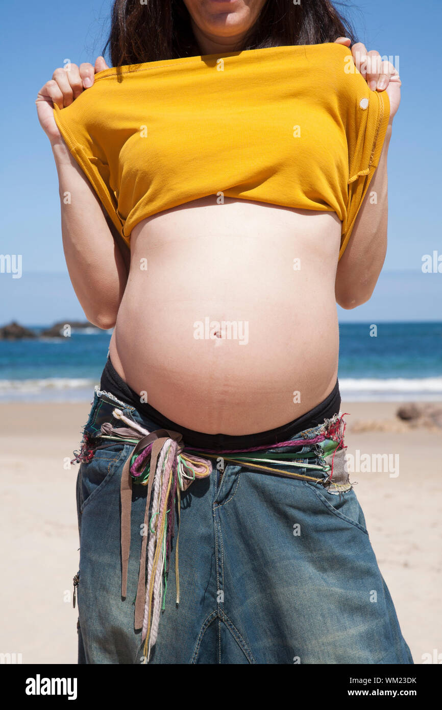 Femme enceinte en montrant son nombril à l'asturien beach Banque D'Images