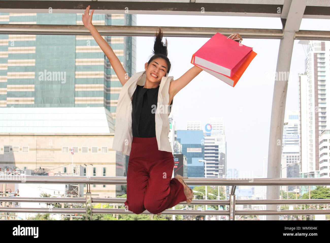 Portrait Of Smiling Young Woman with Shopping Bags sautant Dans Covered Bridge Banque D'Images