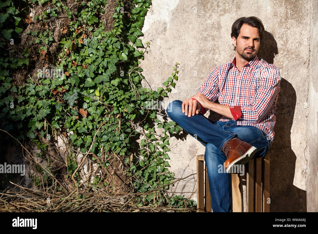 Souriant modèle masculin assis sur des caisses en bois avec les jambes croisées Banque D'Images