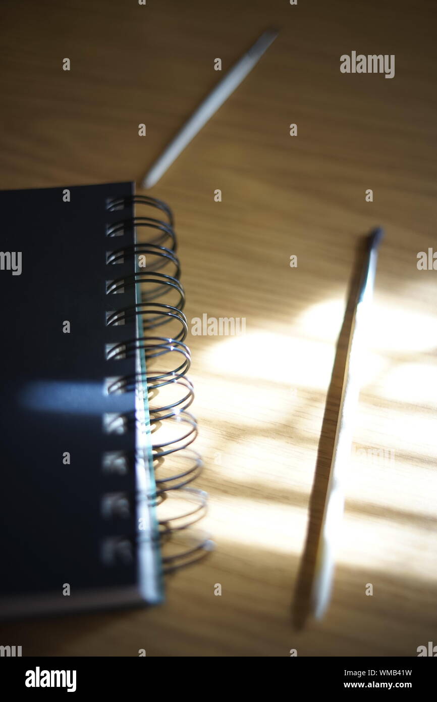 Ordinateur portable noir sur une spirale, pinceau et crayon sur une table avec le soleil et les ombres. Matériaux pour la créativité. Banque D'Images
