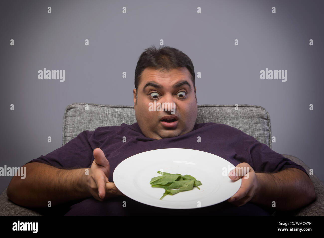 Obèses malheureux homme tenant une assiette avec quelques feuilles  d'épinard et montrant l'expression de choc et de dégoût Photo Stock - Alamy