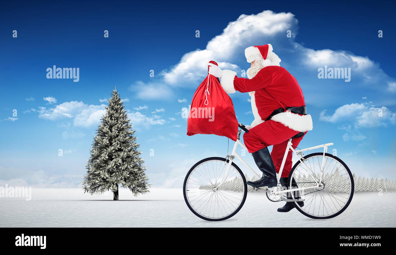 Santa vélo et tenant son sac contre sapin dans paysage de neige Banque D'Images