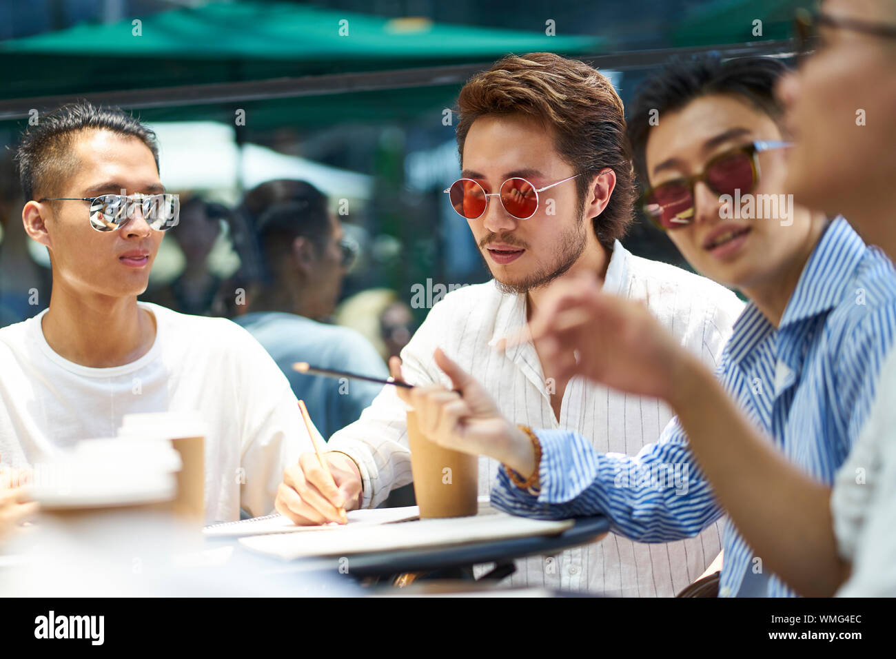 Les jeunes étudiants asiatiques ayant un groupe de discussion à un café-restaurant en plein air Banque D'Images