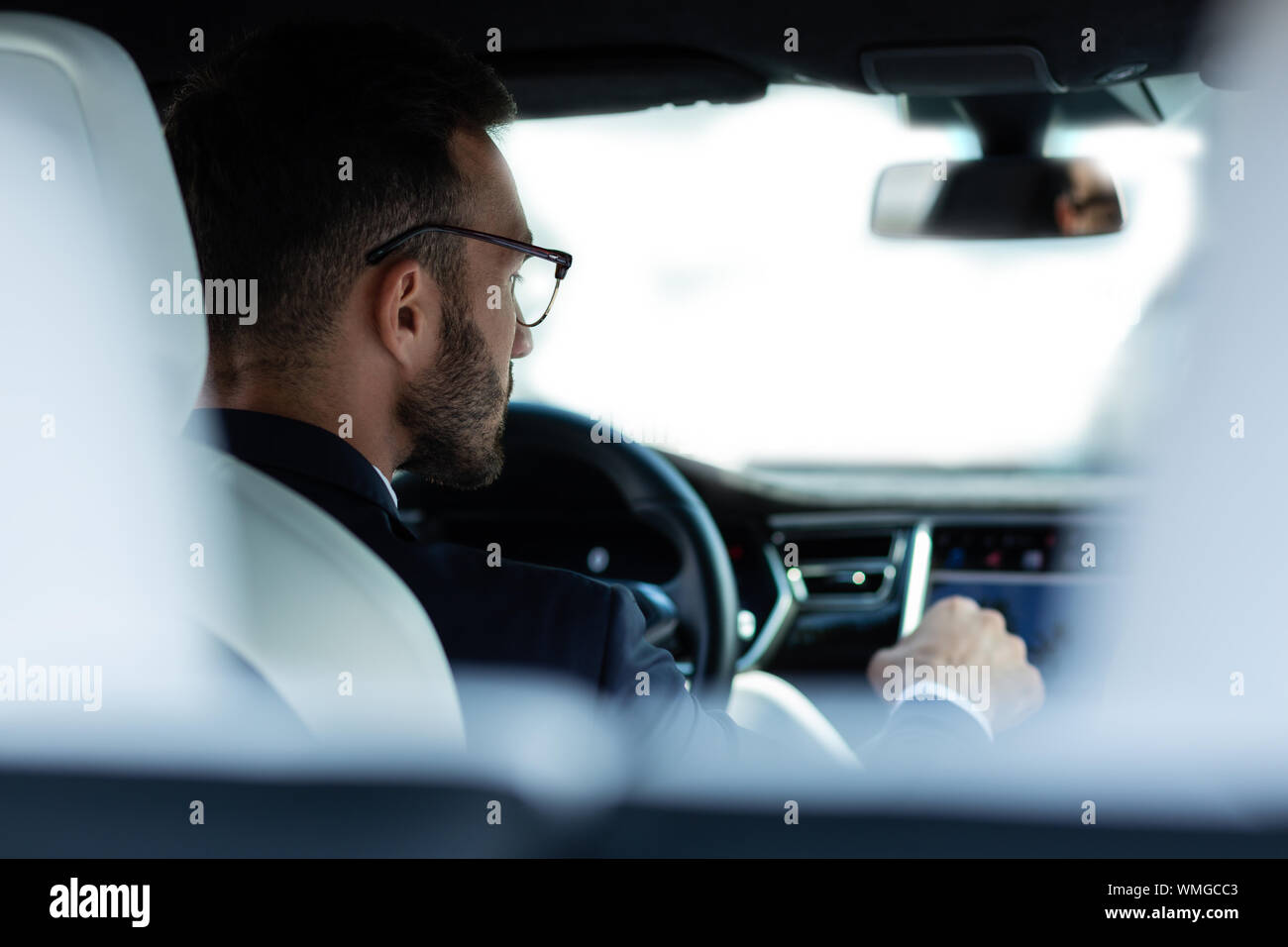 Jeune homme barbu à lunettes assis dans sa voiture Banque D'Images