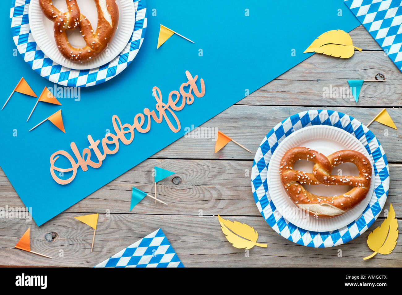 L'Oktoberfest, télévision jeter en bleu, jaune et orange sur table en bois rustique avec du papier bleu propagation, les bretzels sur plaques à usage unique, les épis de blé, des objets de décoration Banque D'Images