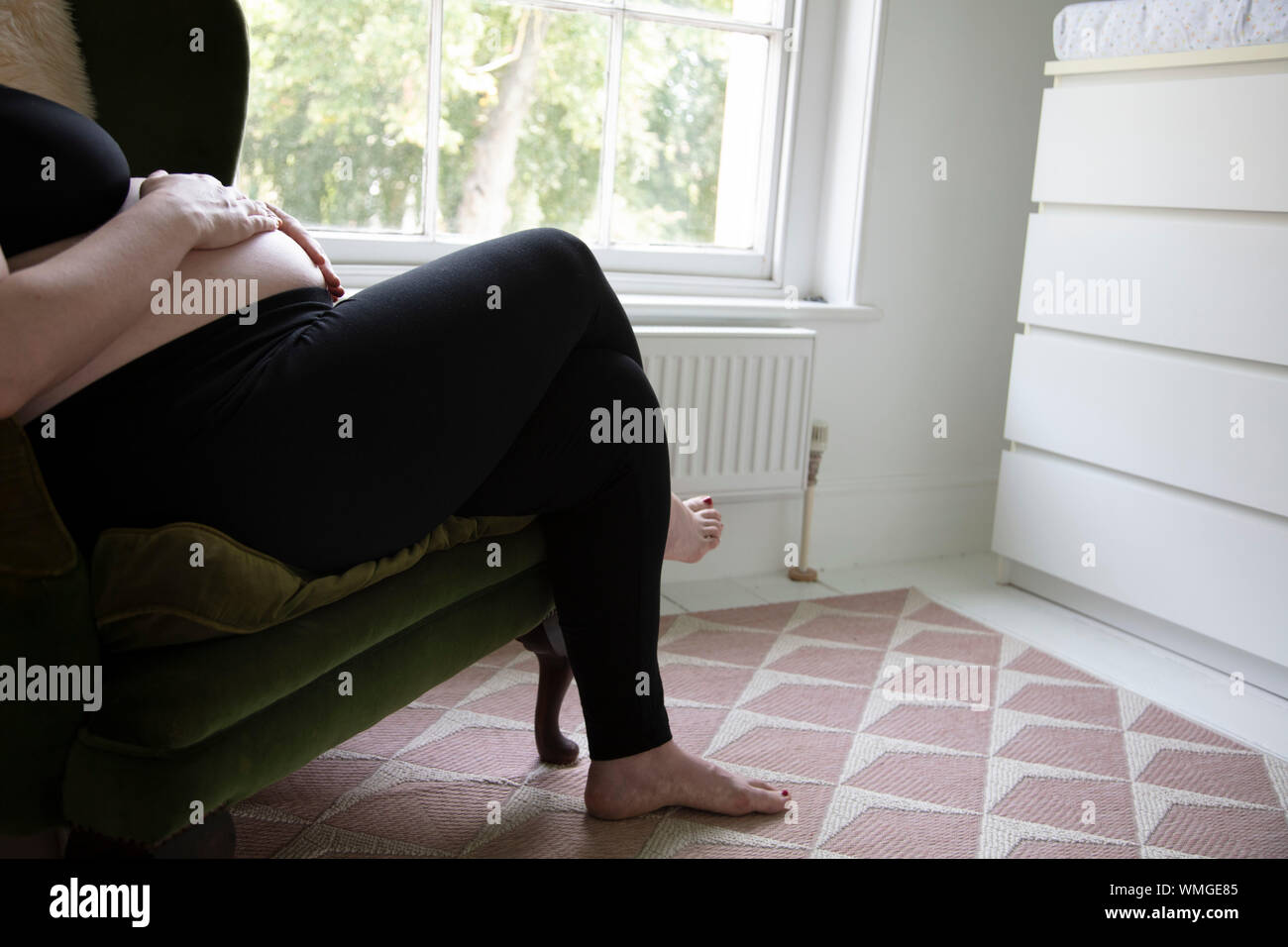 Un prgnant woman holding her baby bump tout en vous relaxant sur une chaise Banque D'Images