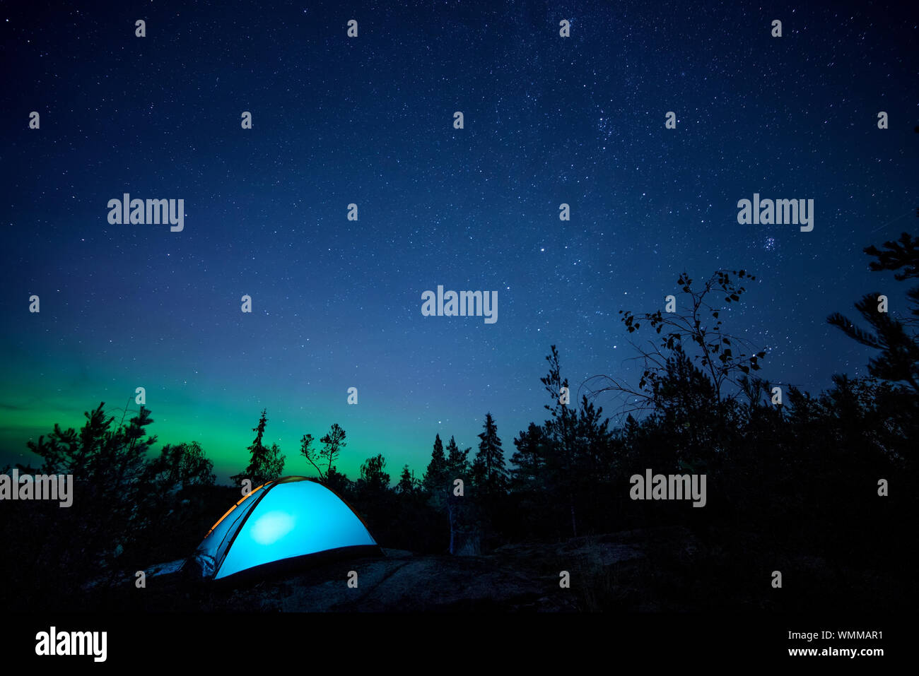 Scène de nuit éclairée avec tente de camping, forêt, ciel étoilé et northern lights. L'exposition longue Banque D'Images