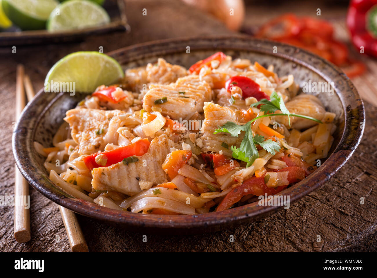 Un bol de poulet délicieux pad thaï avec des nouilles de riz, poivron rouge, carotte, arachide, ciliantro et lime. Banque D'Images