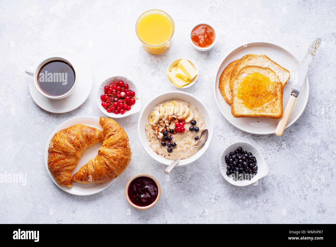 Le petit-déjeuner avec du gruau avec des baies et des noix, des croissants, des toasts avec du beurre et de la confiture, du café et du jus d'orange Banque D'Images