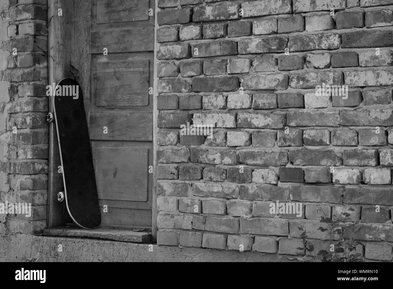 Planche à roulettes penchée contre une vieille porte en bois dans un mur de briques, monochrome Banque D'Images