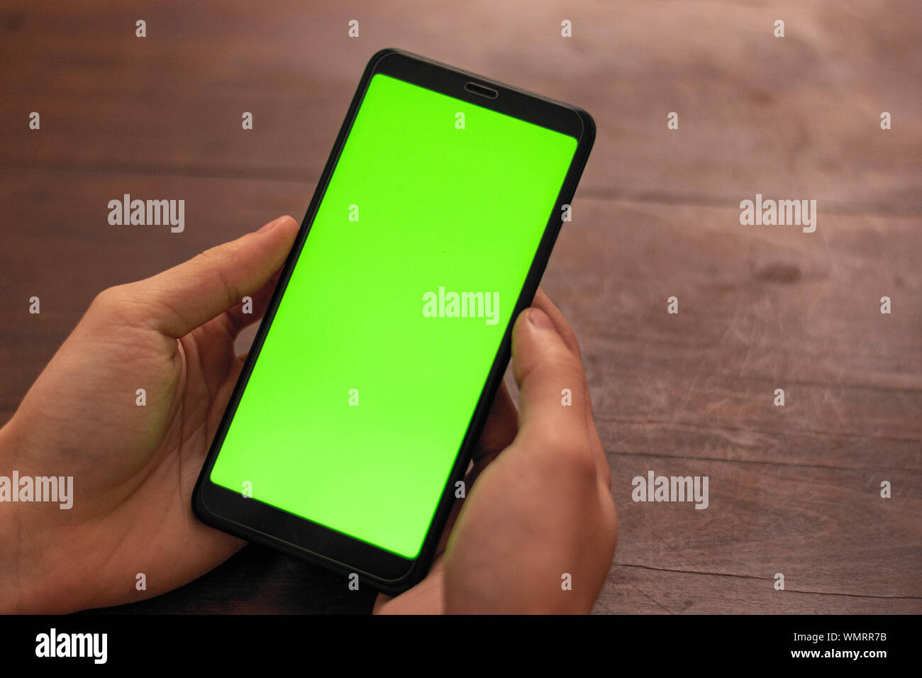 Part des titulaires d'une personne de race blanche non identifié noir smartphone avec un écran vert sur un fond de table en bois Banque D'Images