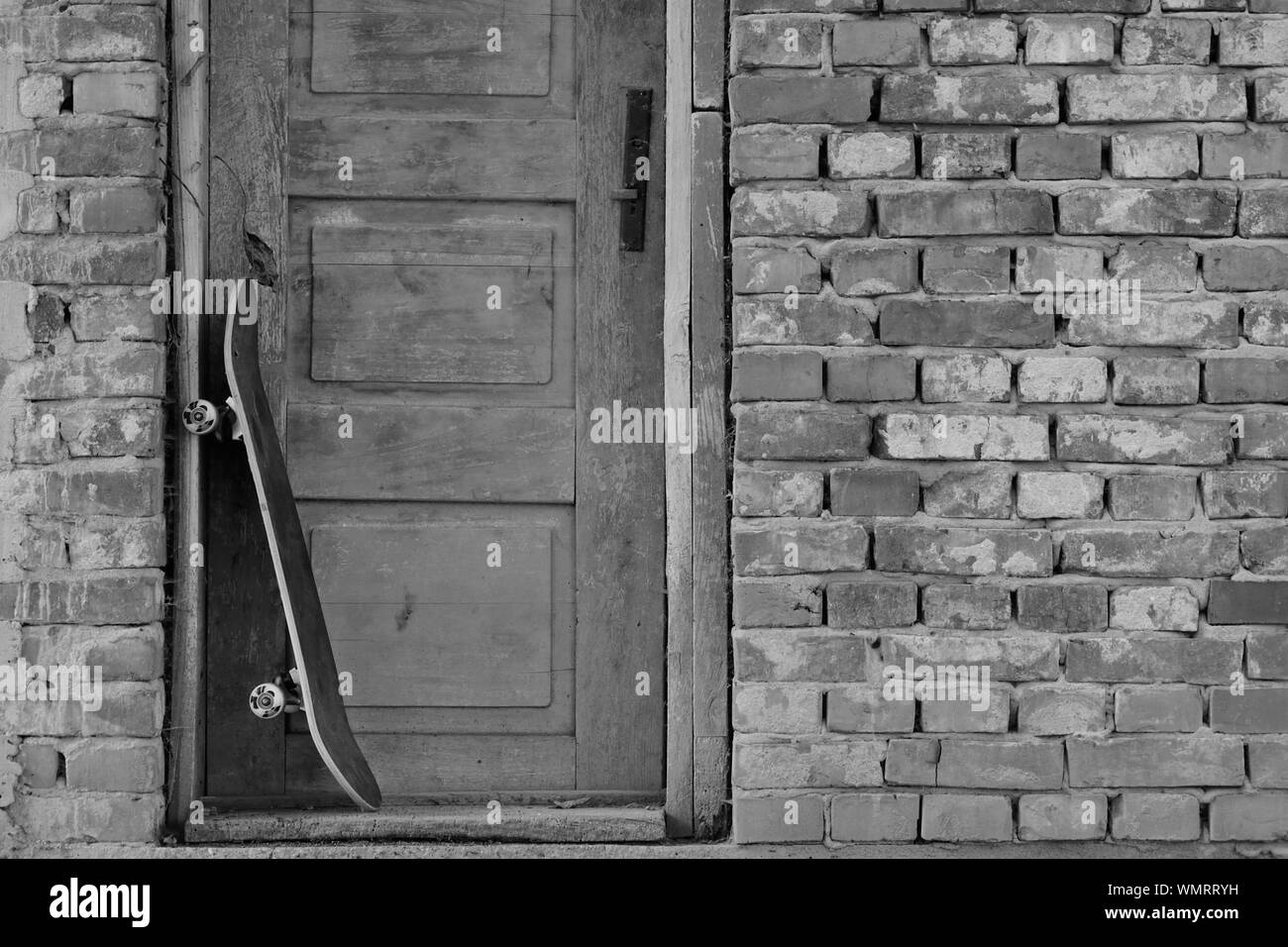Monochrome, Skateboard penchant contre une vieille porte en bois dans le mur de brique Banque D'Images
