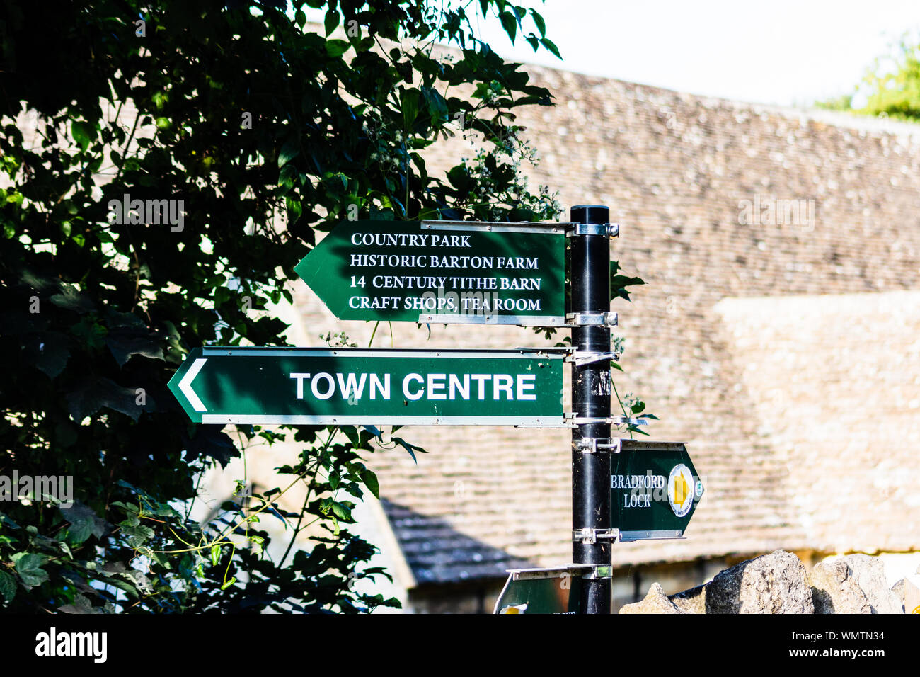 Un poteau de signalisation sur le chemin de halage du canal de Kennet et Avon à Bradford on Avon, donnant des directives à divers endroits, avec la grange dîmière en arrière-plan Banque D'Images